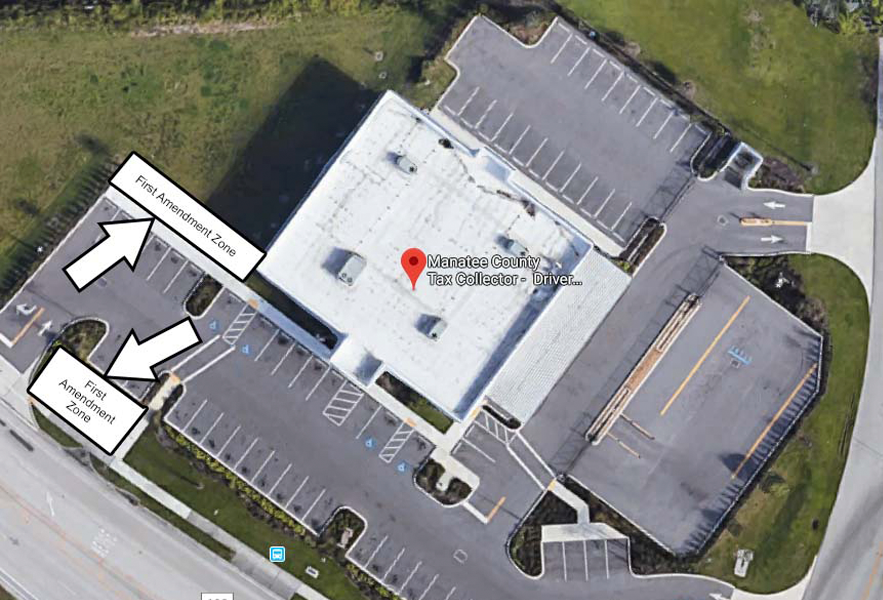 Overhead view of Driver License office. This office has two First Amendment Zones. One zone is a long rectangular area to the west of the building. It runs northwest and southeast and has grassy areas on its west and north sides, the building on its east side, and a sidewalk on its south side. The other zone is a rectangular area to the southwest of the building. It has sidewalks on its east and south sides, a parking lot entrance and exit on its west side, and a grassy area and parking spaces on its north side.